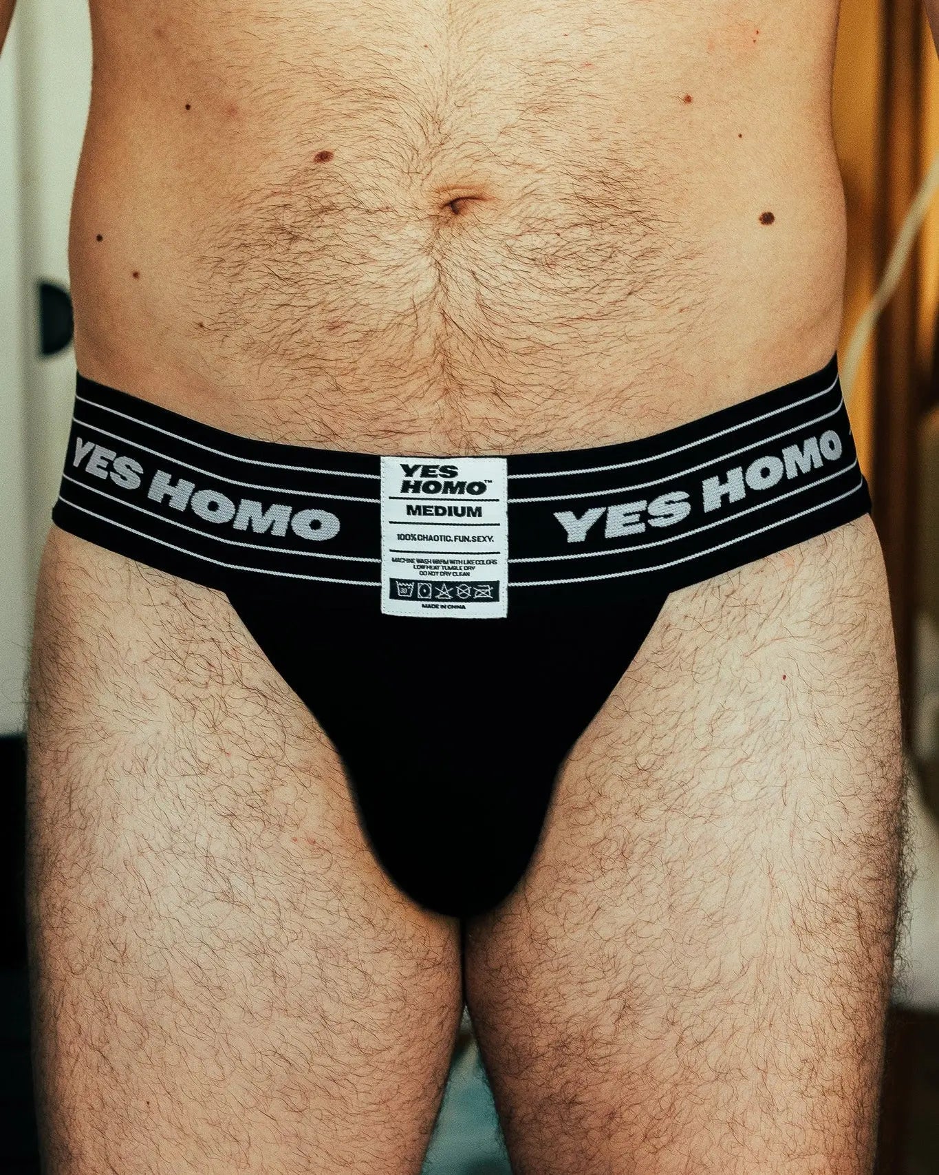 Black underwear with 'YES HOMO' branding on a person against a blurred background