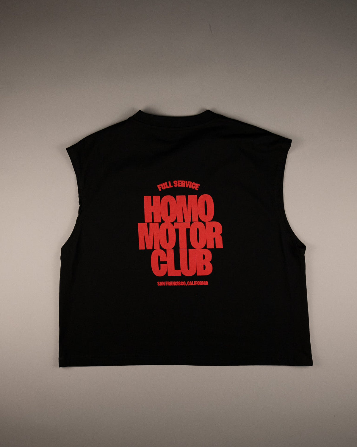 A black sleeveless crop top with a bold red graphic print reading 'HOMO MOTOR CLUB' on the back, laid flat against a neutral gray background.
