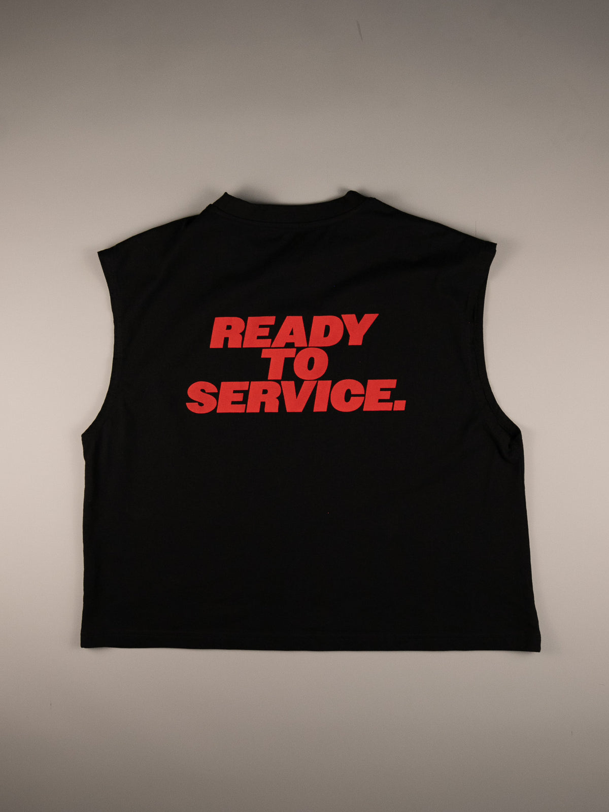 A black sleeveless crop top with the phrase 'READY TO SERVICE.' printed in bold red letters across the chest, laid flat against a neutral gray background.